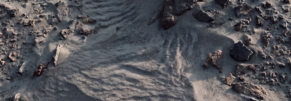 Wind-rippled dust and dark mineral fragments, seen from above.